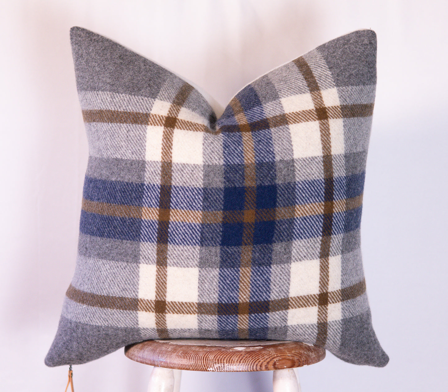 Plaid pillow with blue, gray, and cream colors on a wooden stool against a white background