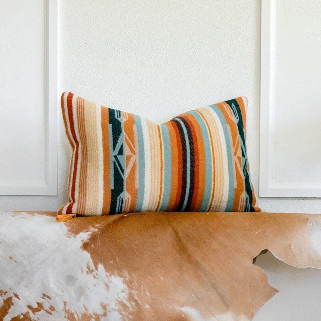 Colorful striped pillow on a wooden bench with a white wall background
