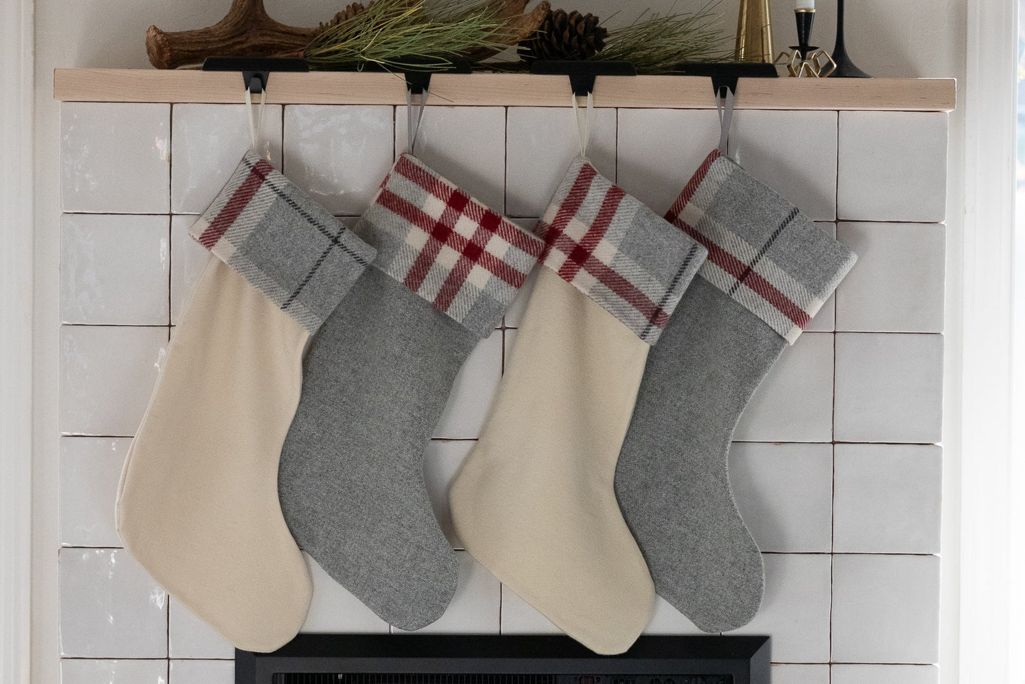 Four Christmas stockings with plaid trim hanging on a fireplace mantle.