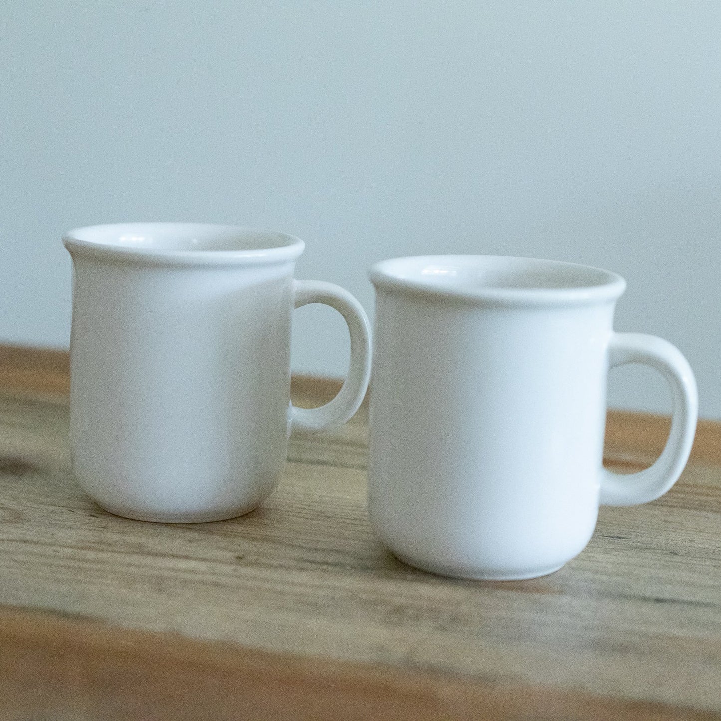 Two white ceramic mugs on a wooden surface with a light gray background