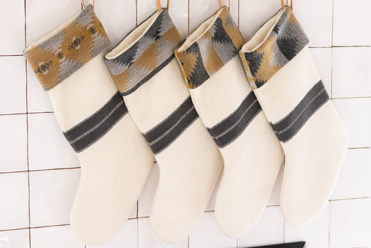 Four white stockings with brown and gray patterns hanging on a tiled wall.