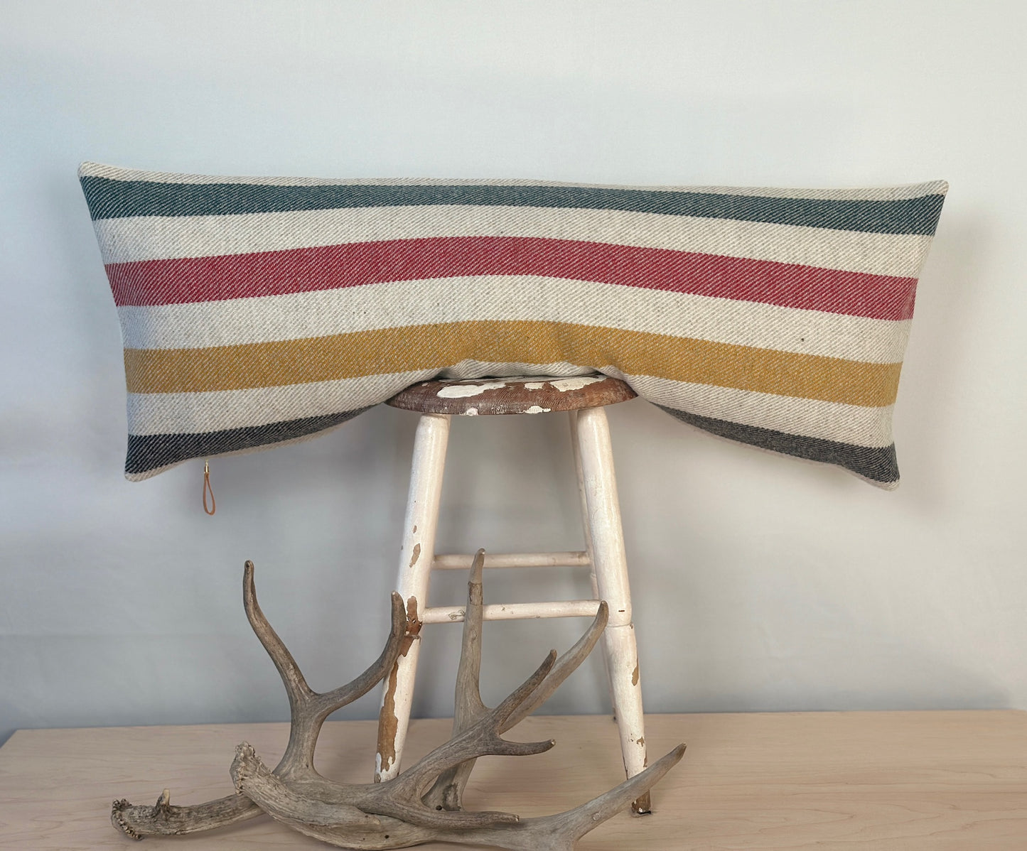 Striped pillow on a stool with antlers in front against a light background