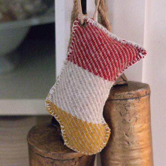 Wool stocking made with Pendleton Glacier Wool that has a red and yellow pattern hanging on a rustic wooden post.