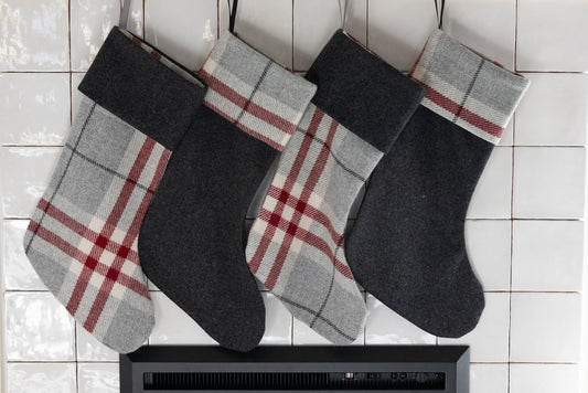 Two plaid stockings hanging above a fireplace on a tiled wall.