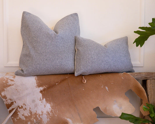 Two gray pillows on a rustic wooden surface with a cowhide rug and plant in the background.