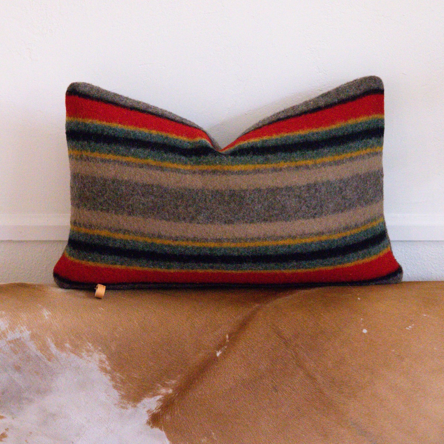 Colorful striped pillow on a worn-out brown couch with a white wall background