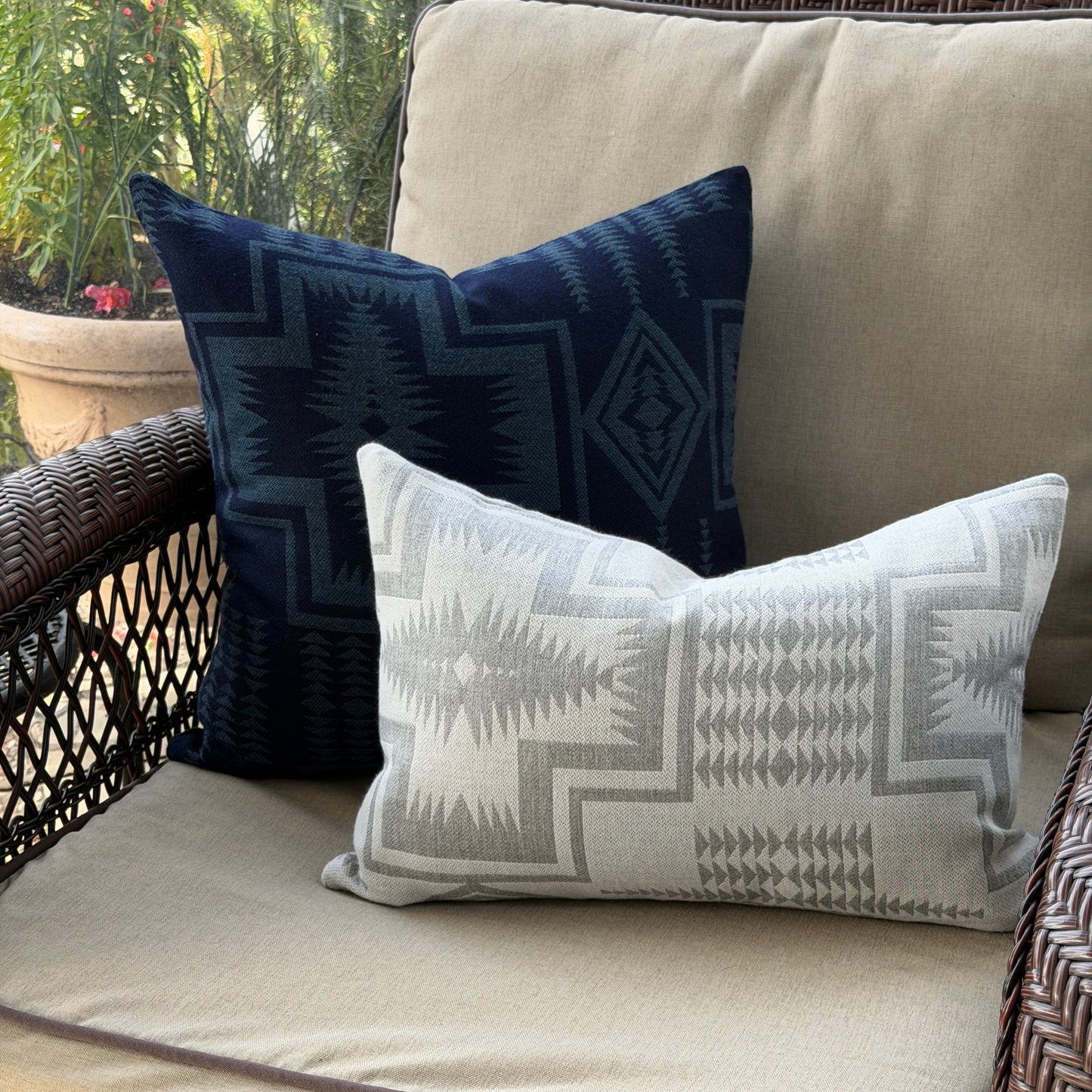 Two patterned pillows on a beige outdoor sofa with a blurred natural background