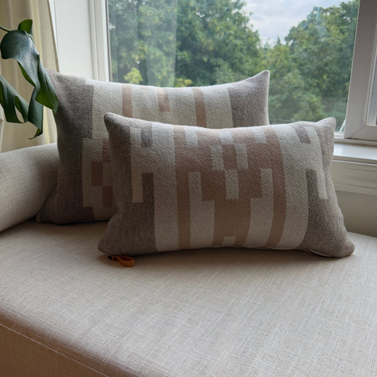 Two patterned cushions on a light-colored sofa next to a window with a view of trees.