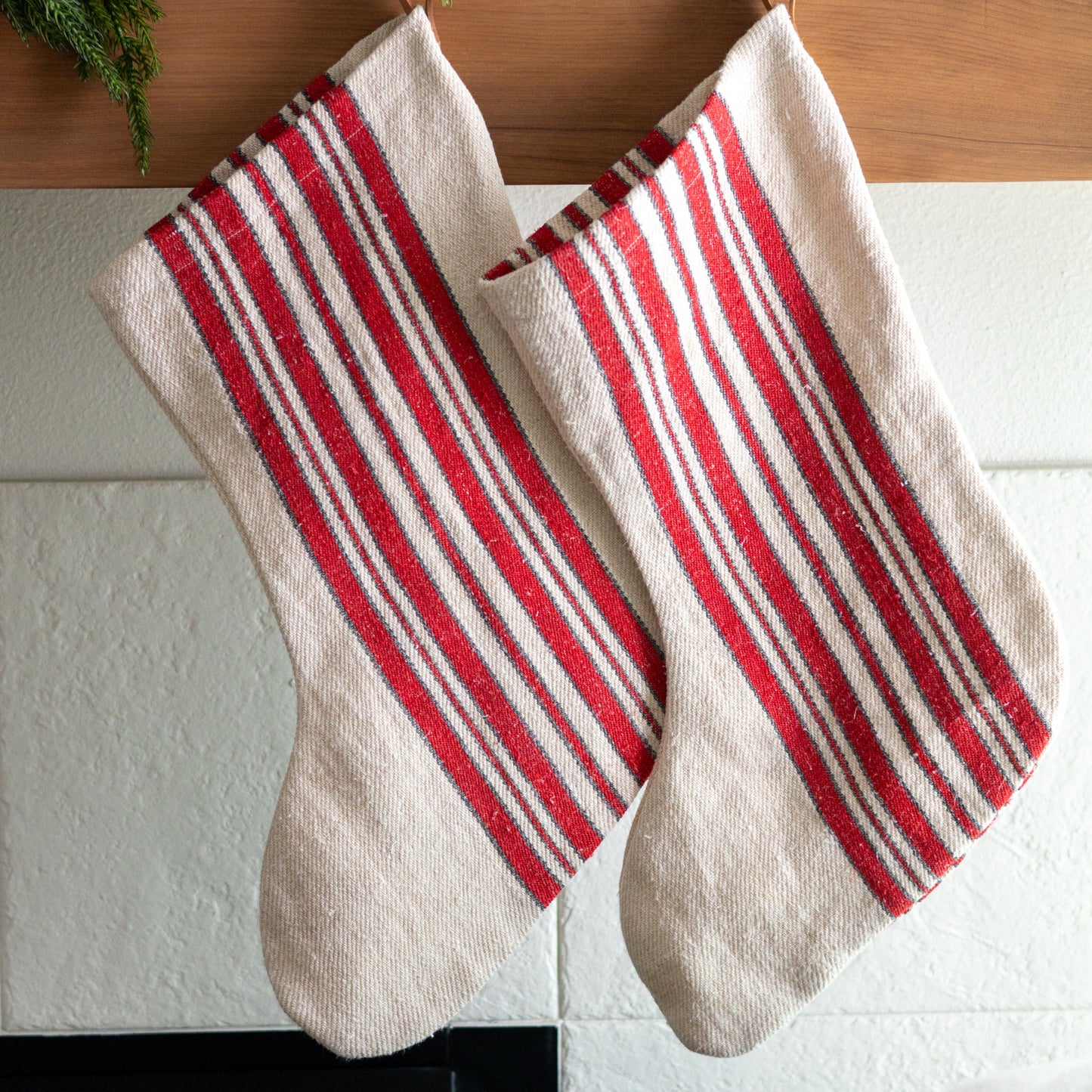Red and white striped stockings hanging on a wooden mantel with greenery.