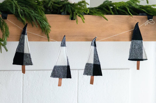 Decorative Christmas trees on a string with greenery above a white fireplace.