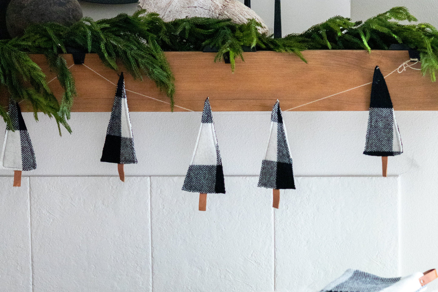 Decorative Christmas tree garland on a mantel with a white wall and chair in the background.