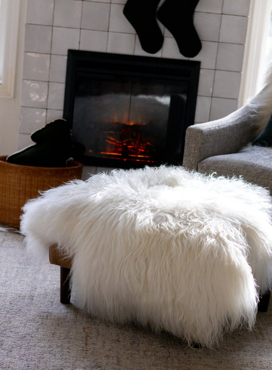 White fluffy ottoman in front of a fireplace with stockings hanging above.