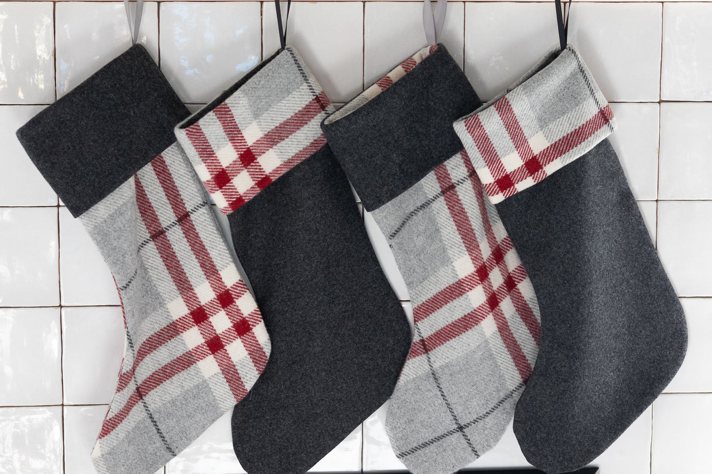 Four plaid Christmas stockings hanging on a tiled wall.