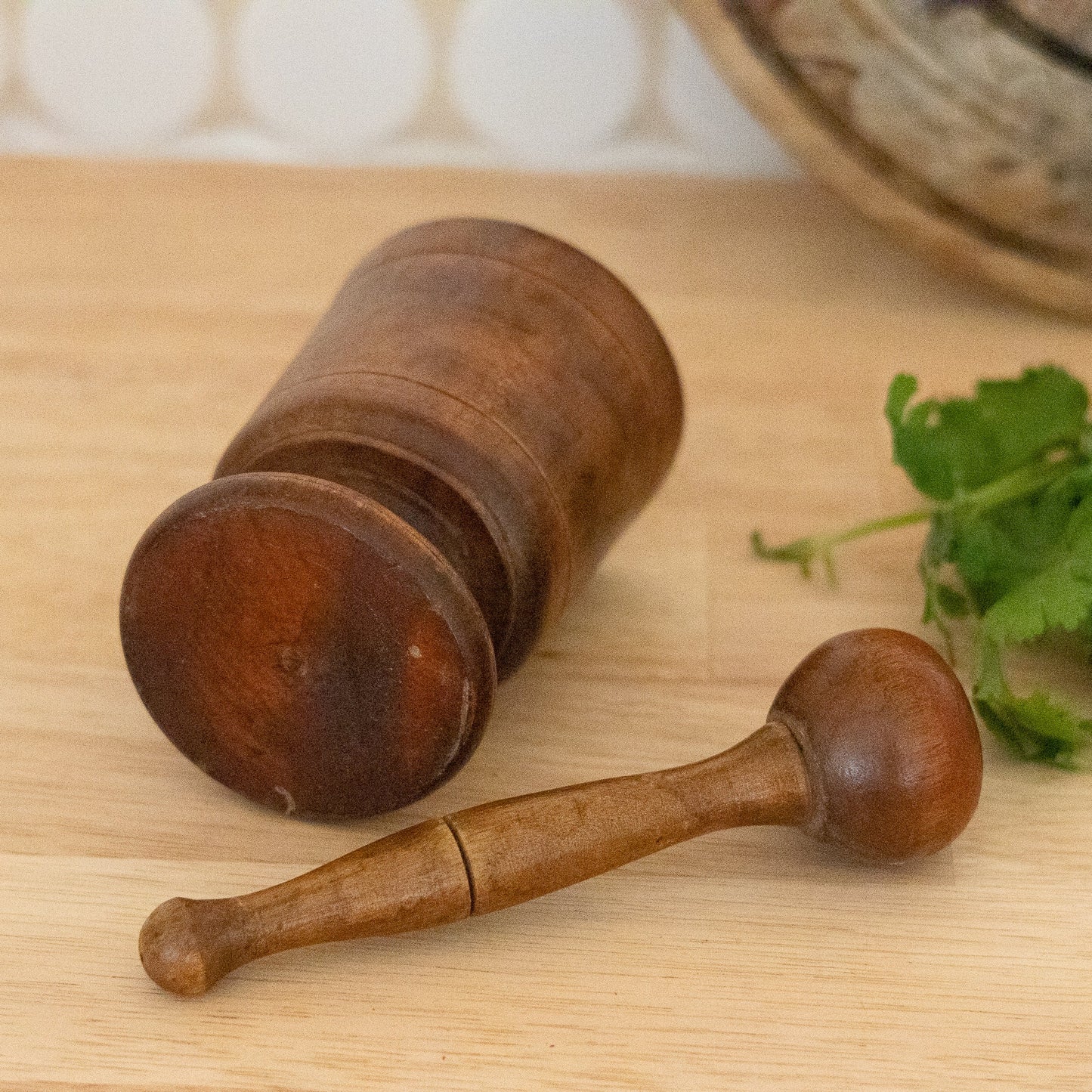 Wooden mortar and pestle on a wooden surface with herbs in the background