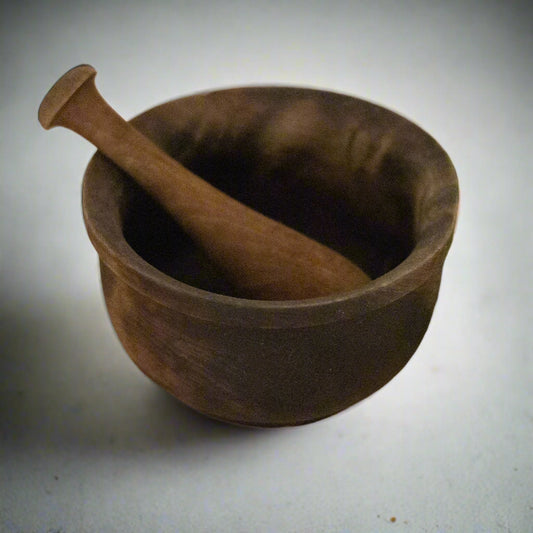 Wooden mortar and pestle on a wooden surface with fresh herbs.