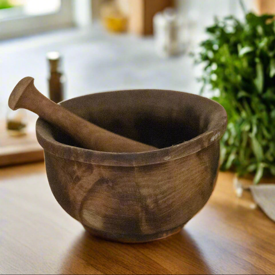 Wooden mortar and pestle on a wooden surface with herbs in the background