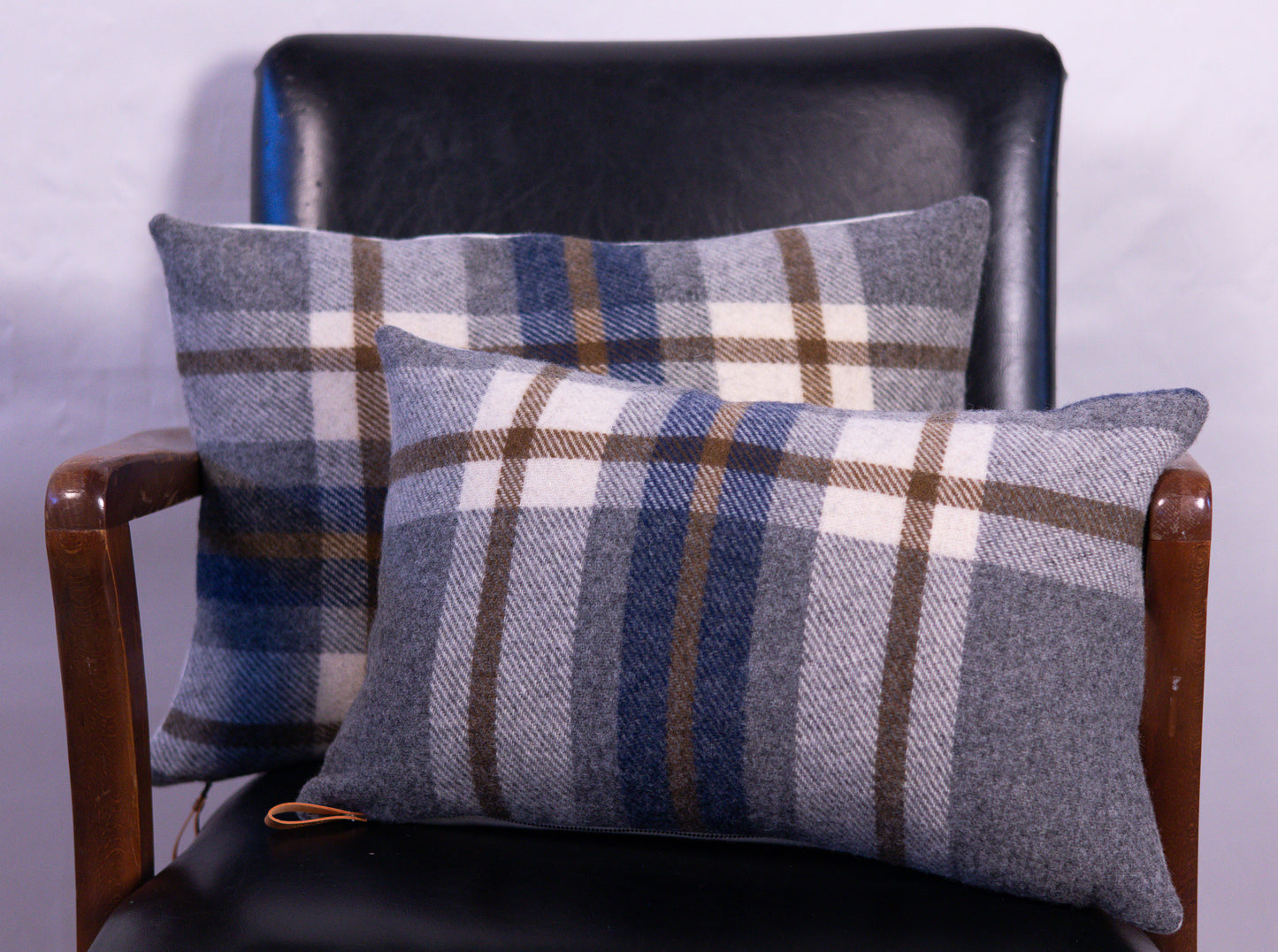 Two plaid cushions on a black leather chair with a white background