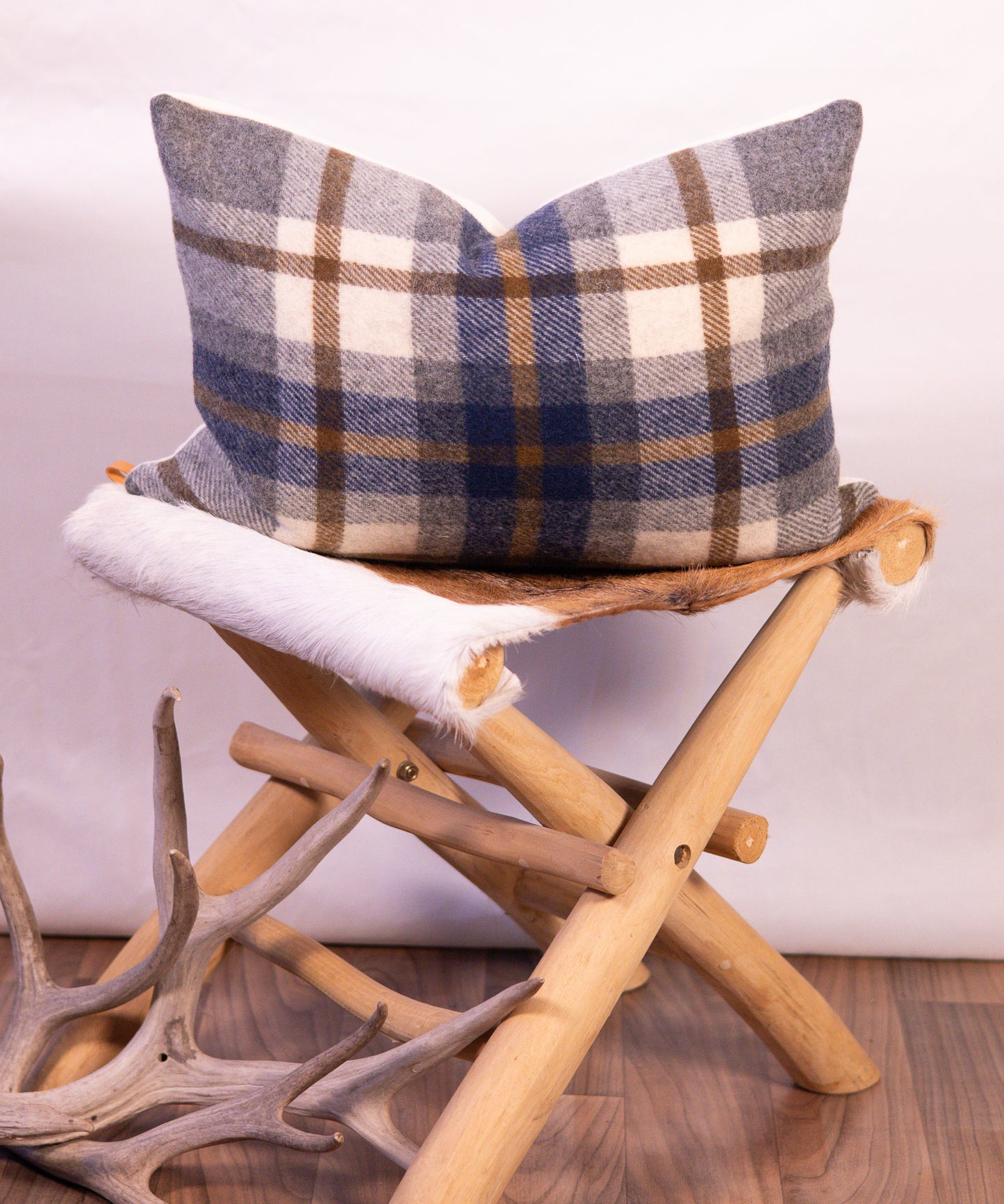 Plaid pillow on a wooden stool with antlers in the foreground