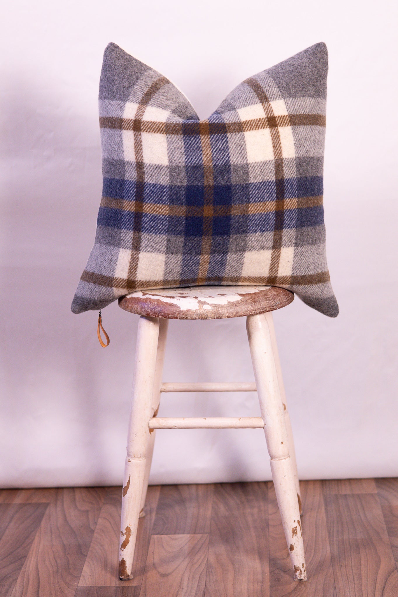 Plaid pillow on a wooden stool against a white wall
