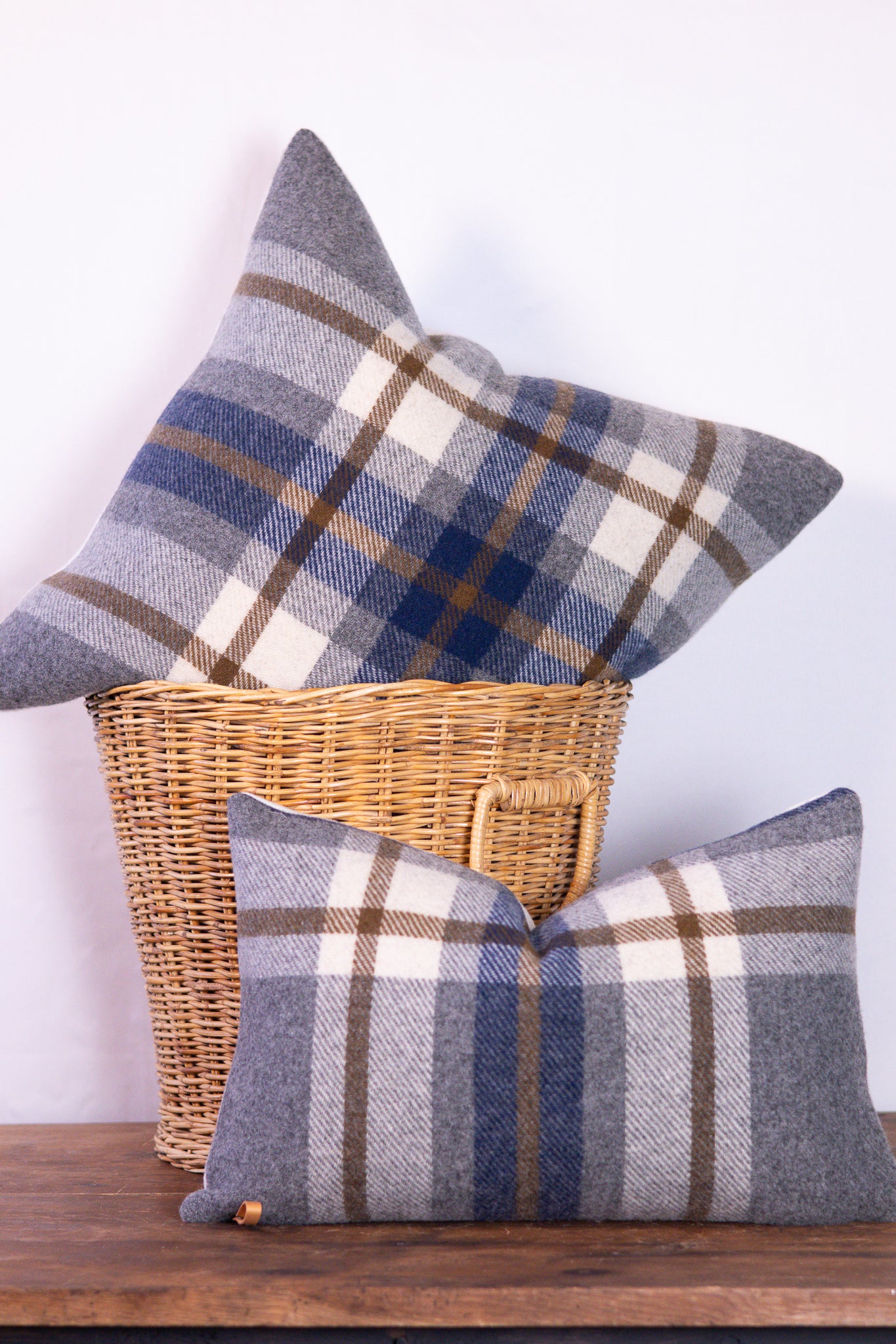 Plaid pillows in a wicker basket on a wooden surface with a white background