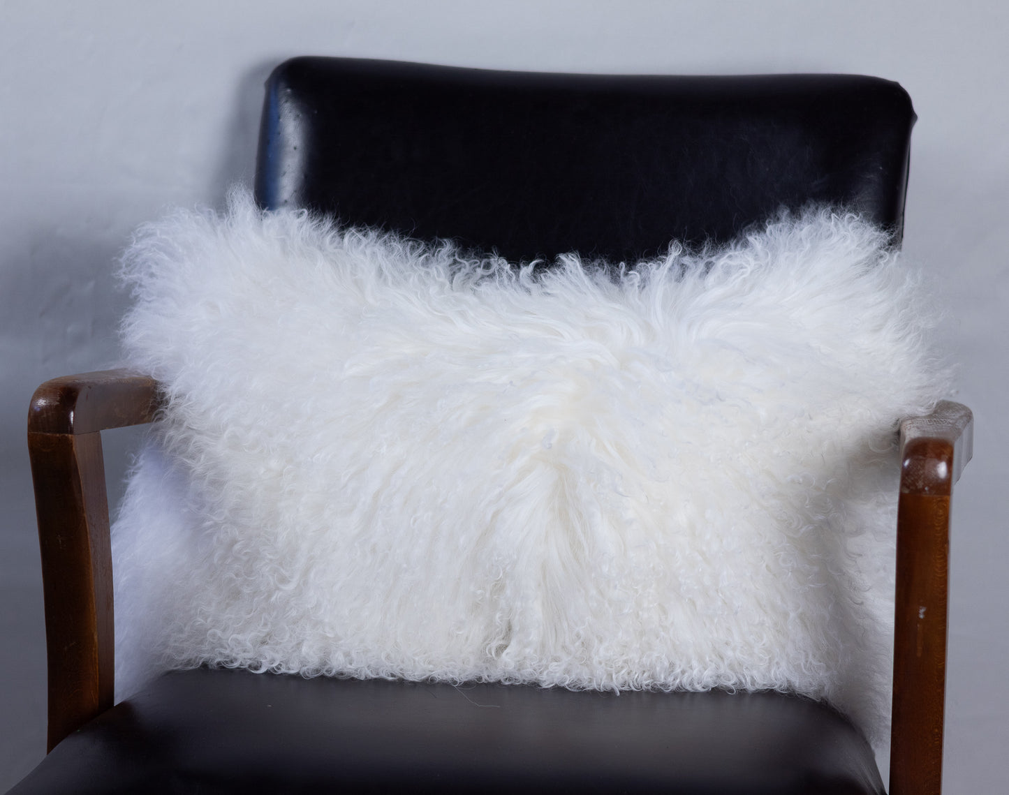 White fluffy pillow on a black chair against a gray background