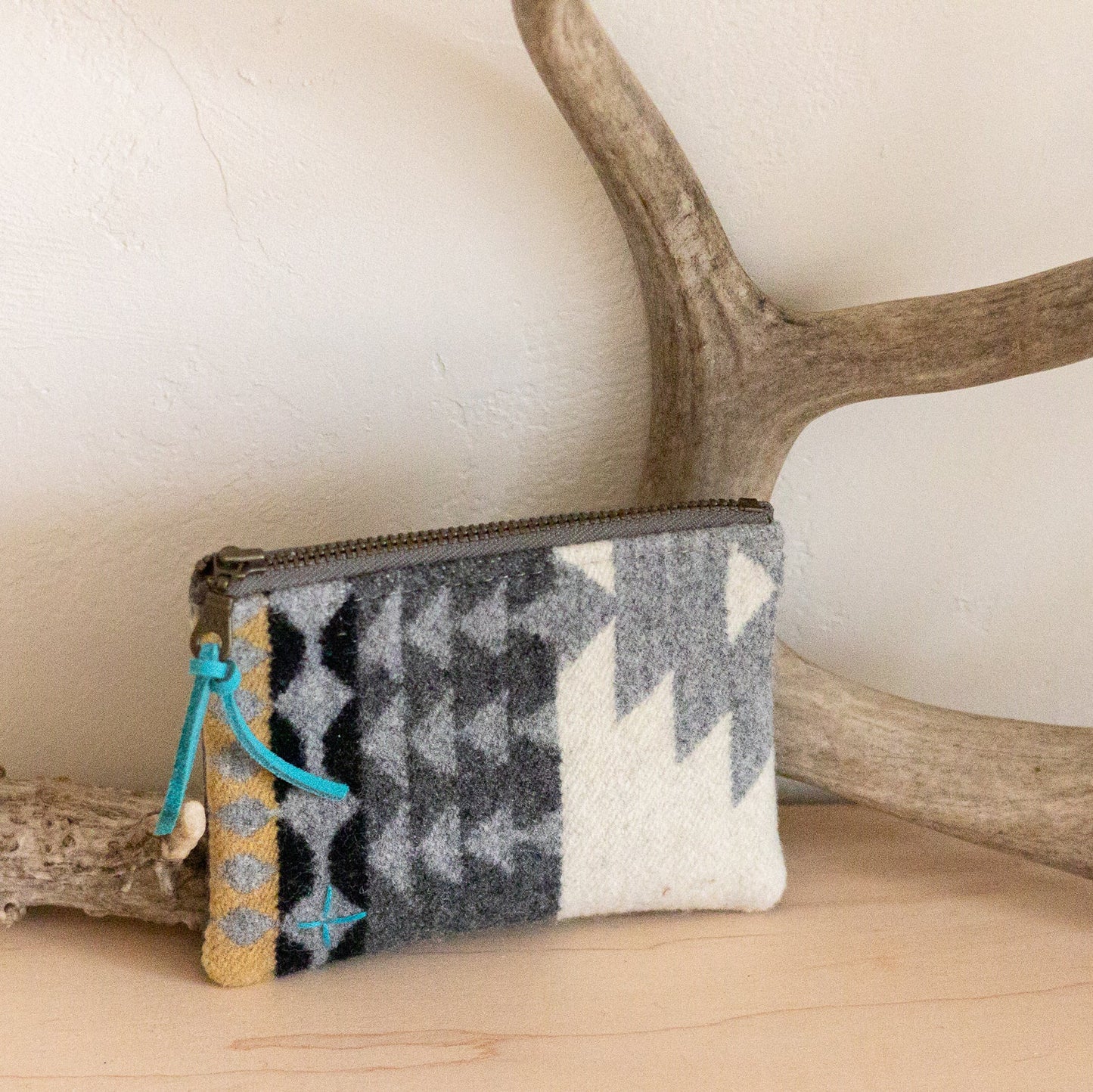 Small pouch with a patterned design on a wooden surface with antlers in the background