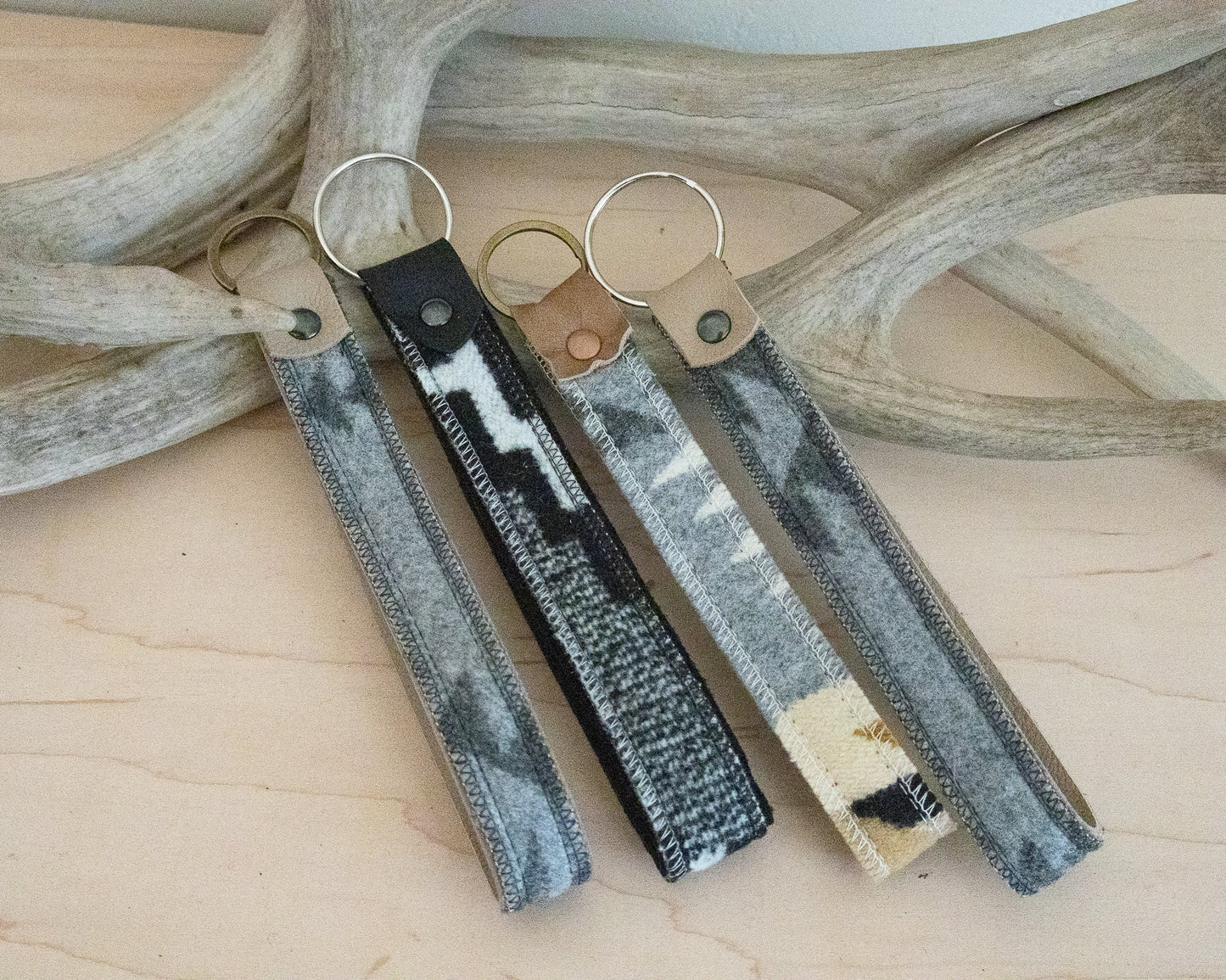 Three keychains with different patterns on a wooden surface with antlers in the background