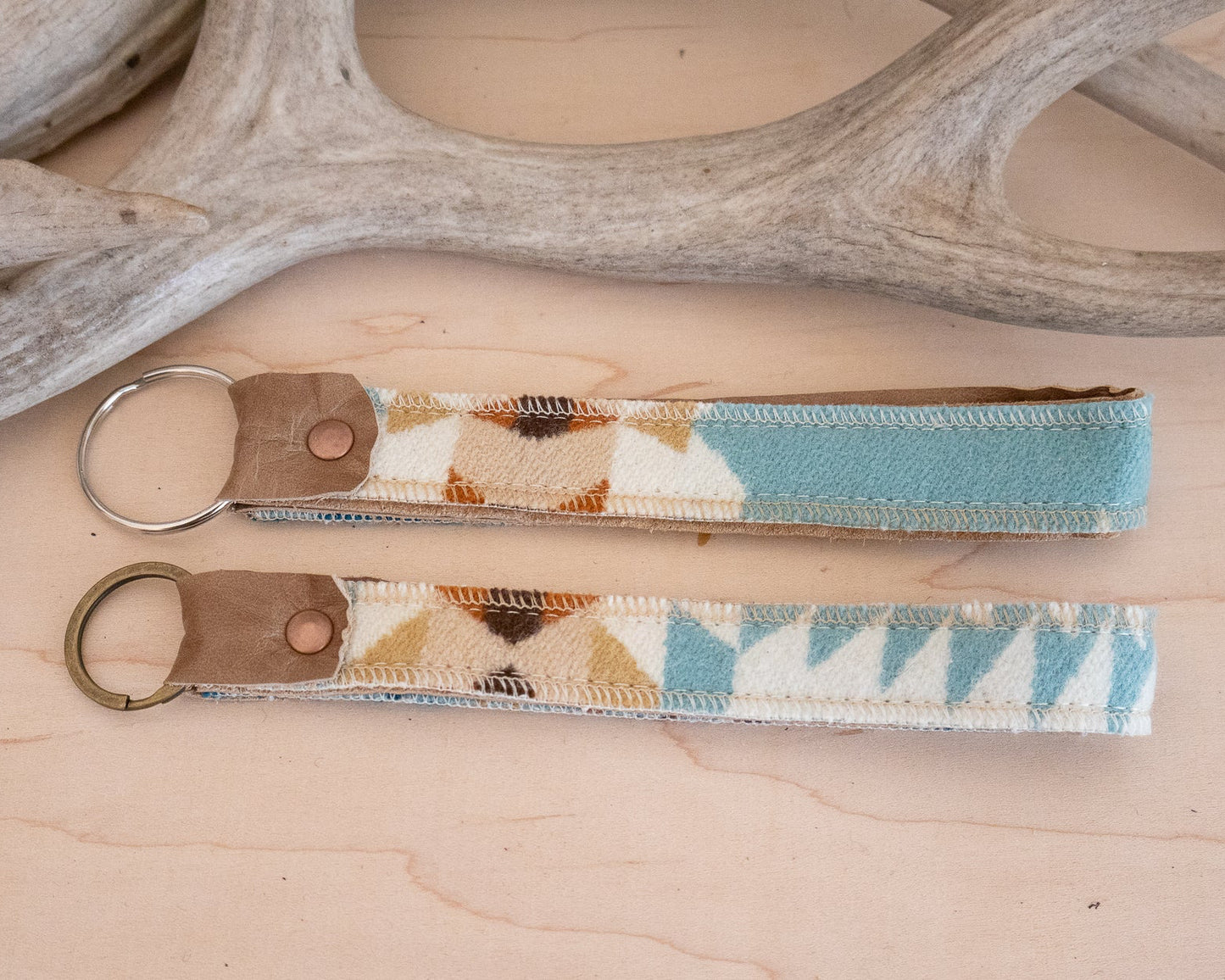 Two keychains with patterned straps on a wooden surface with antlers in the background