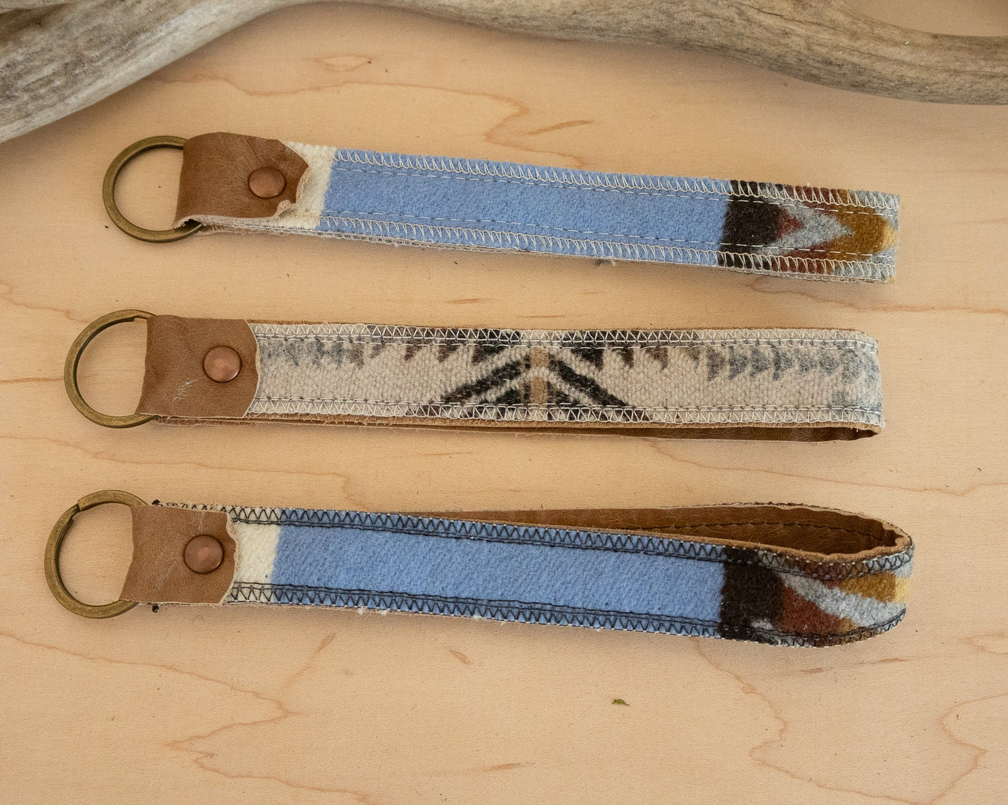 Three fabric keychains with leather ends on a wooden surface