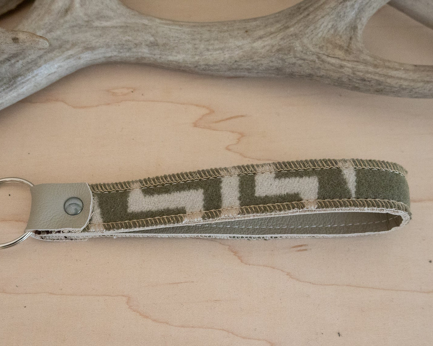 Keychain with a geometric pattern on a wooden surface with antlers in the background