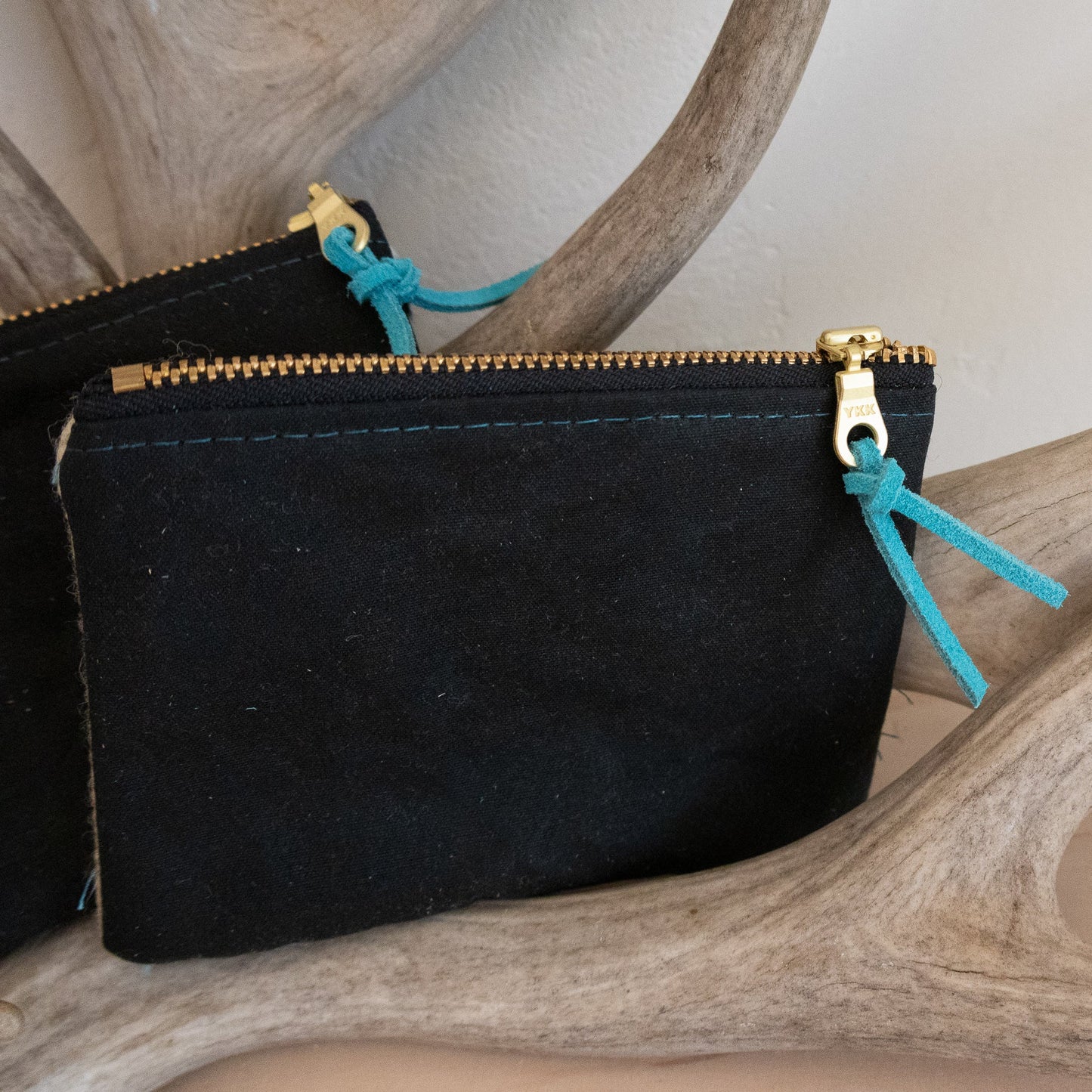 Black pouch with gold zipper and blue drawstrings on a wooden surface