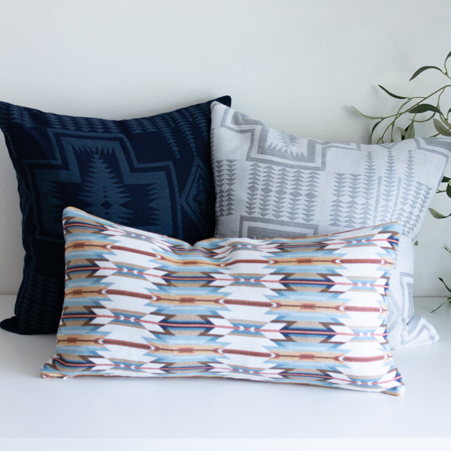 Three patterned pillows on a white surface with a plant in the background