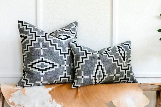 Two patterned pillows on a wooden bench with a plant in the background