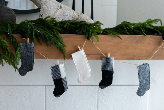 Miniature Christmas stockings hanging on a line against a white wall with greenery.