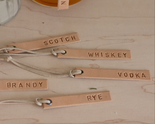 Set of leather tags labeled with different alcoholic beverages on a wooden surface