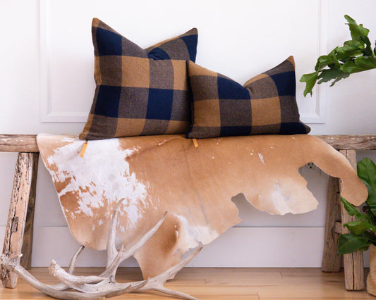 Plaid pillows on a wooden bench with a cowhide rug and plants in the background