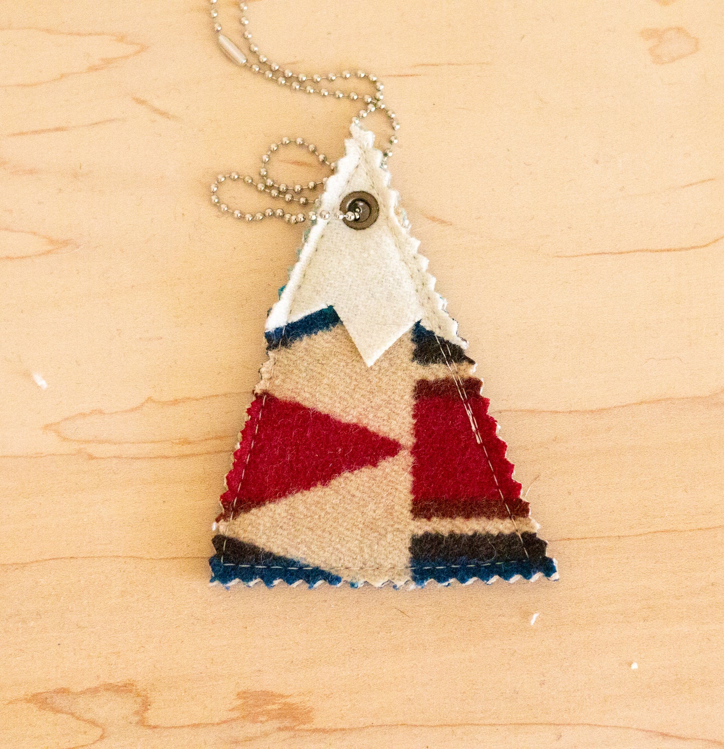 Triangular pendant with red, blue, and beige pattern on a wooden surface