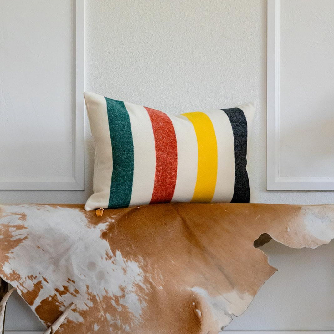 Decorative pillow with striped pattern on a wooden surface with cowhide rug and antlers.