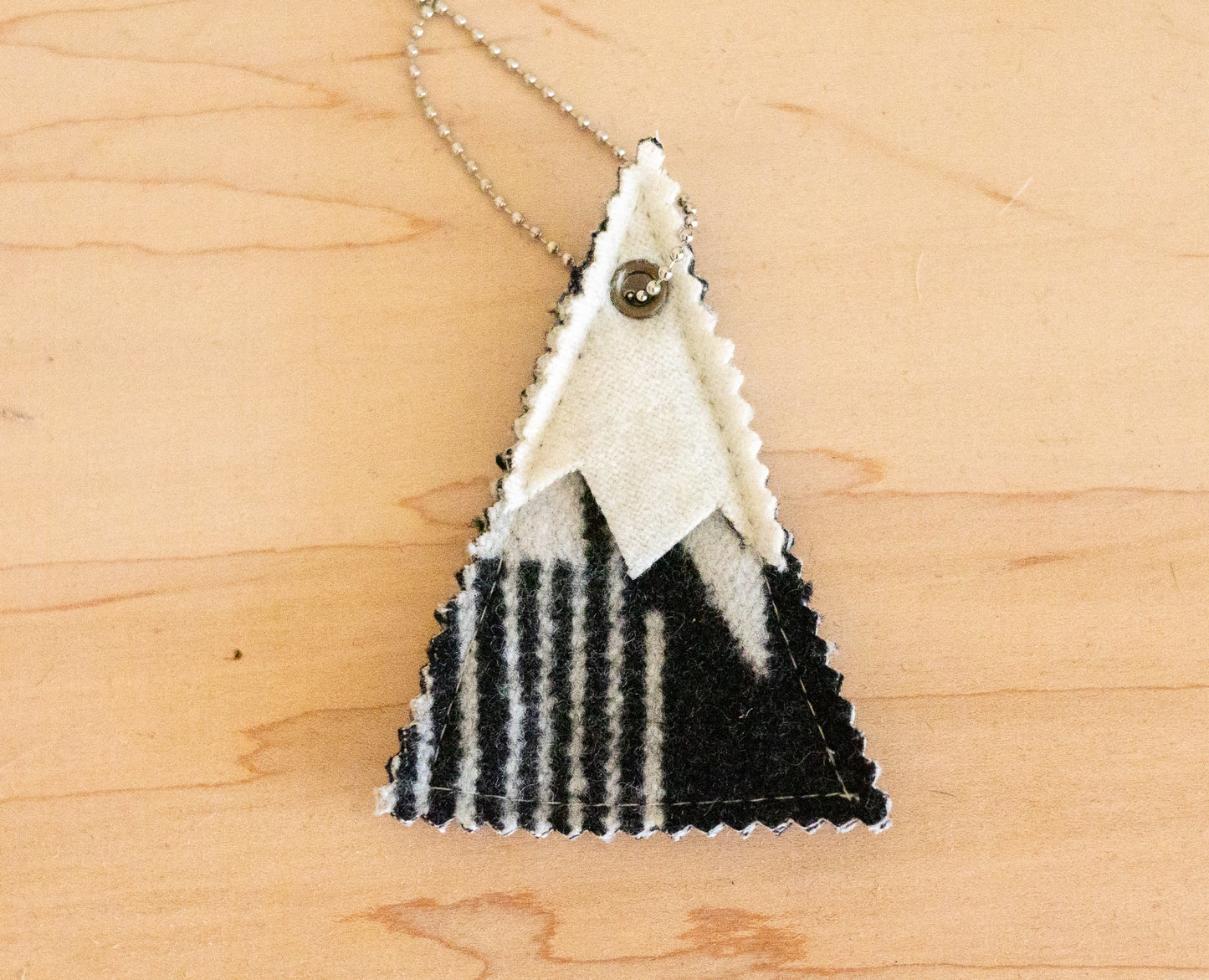Triangular wool air freshener with black and white pattern on a wooden surface