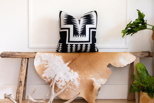 Decorative pillow with geometric pattern on a wooden bench with cowhide rug