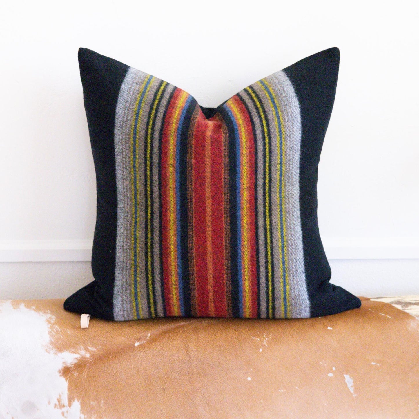 Striped pillow with black, red, and multicolor pattern on a wooden bench.