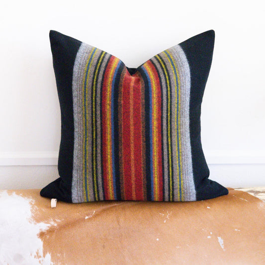 Striped pillow with black, red, and multicolor pattern on a wooden bench.