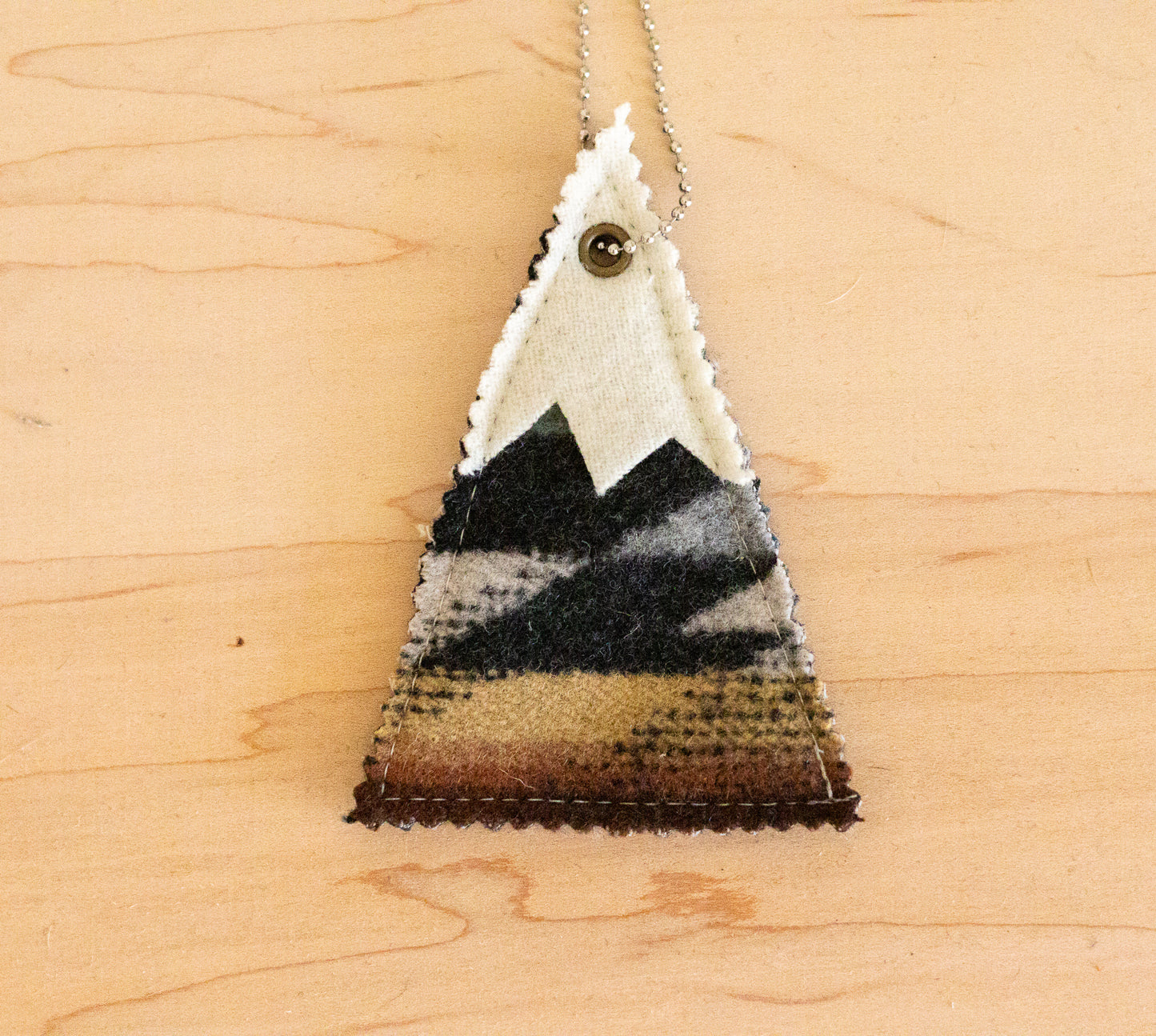 Triangular pendant with mountain design on a wooden surface