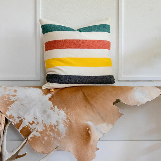 Striped pillow on a wooden surface with a cowhide rug and plant in the background