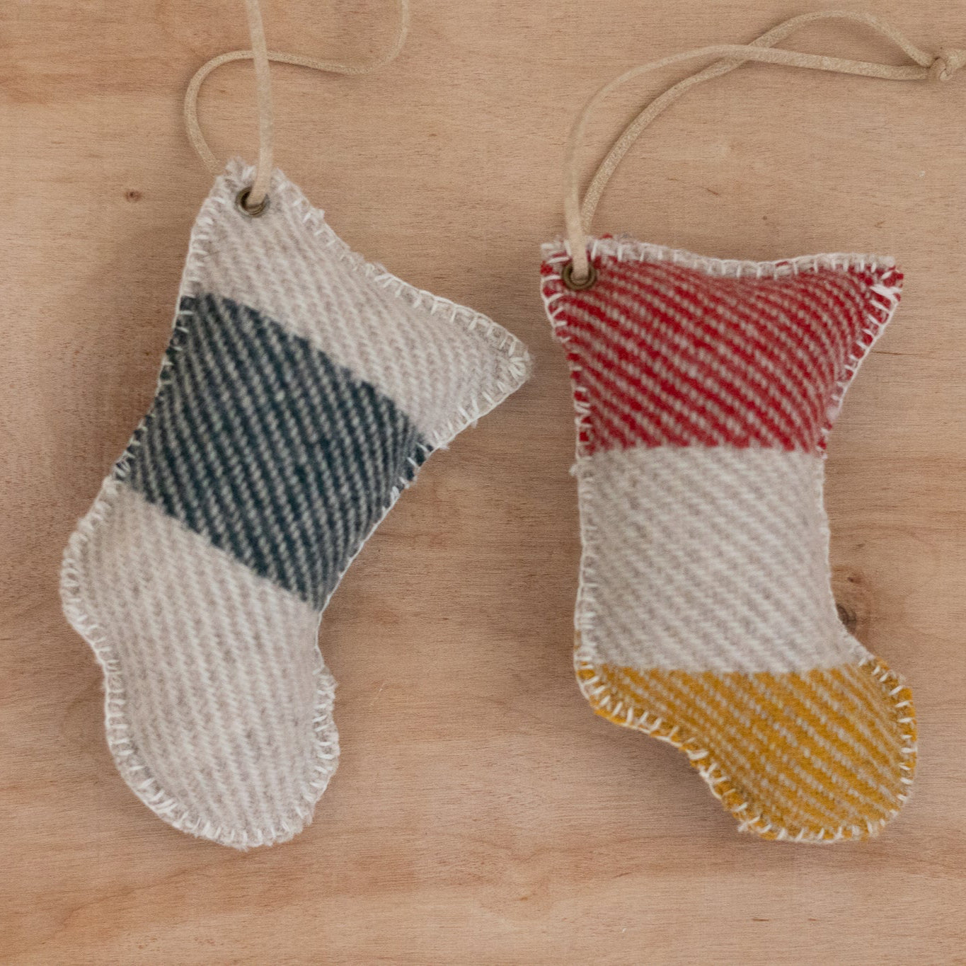 Two small fabric stockings with plaid patterns hanging on a wooden surface.