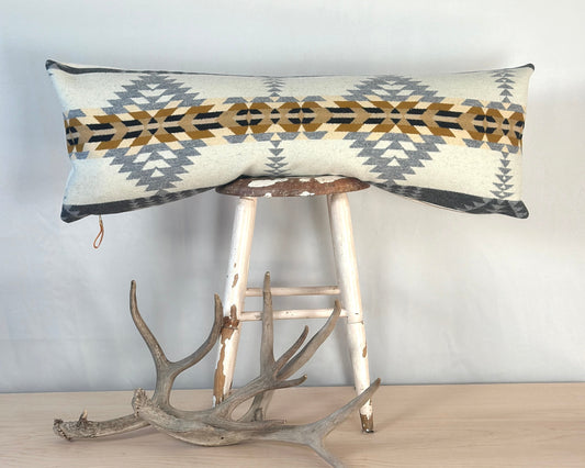 Decorative pillow with geometric pattern on a stool with antlers against a plain background