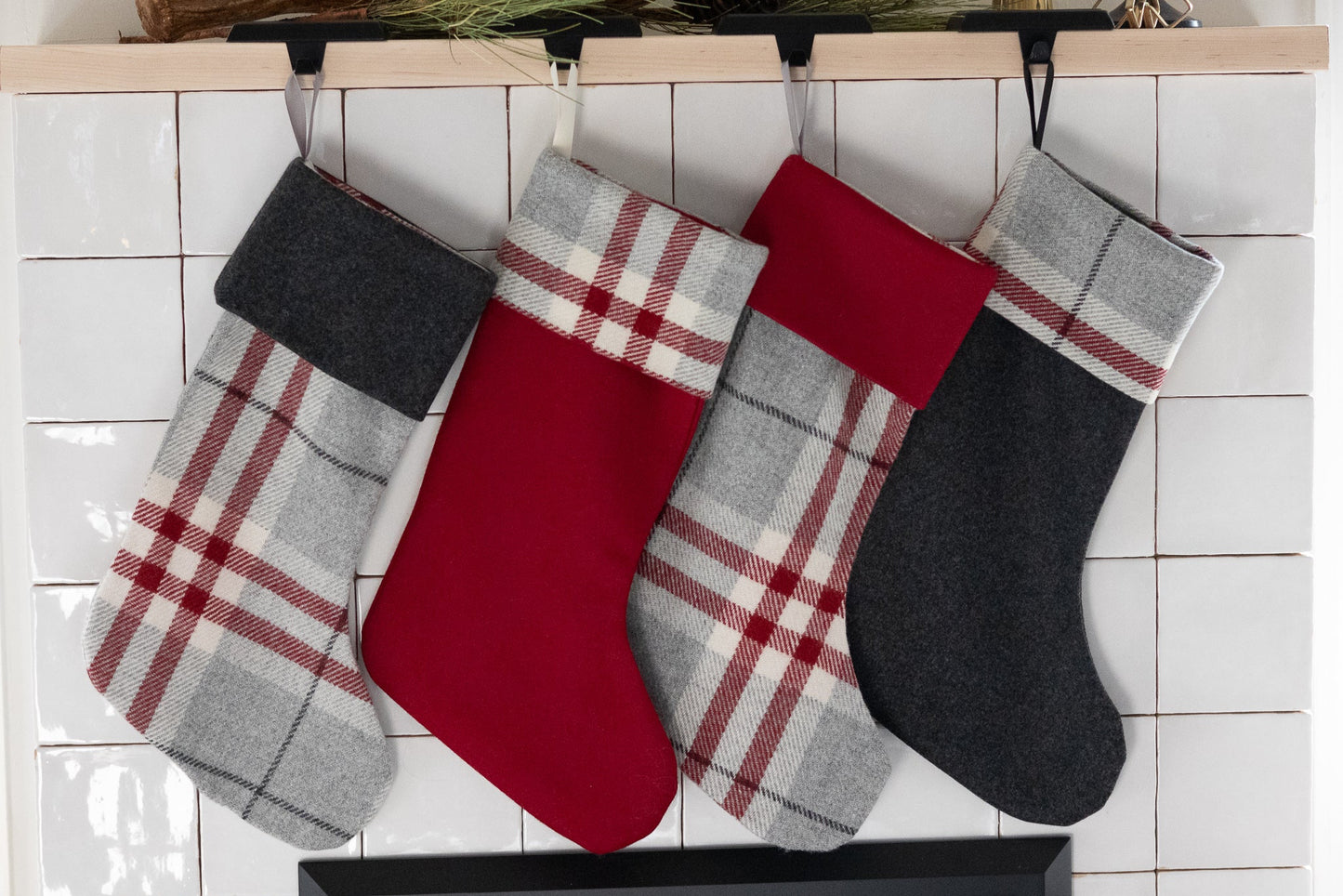 Four plaid Christmas stockings hanging on a fireplace mantle.