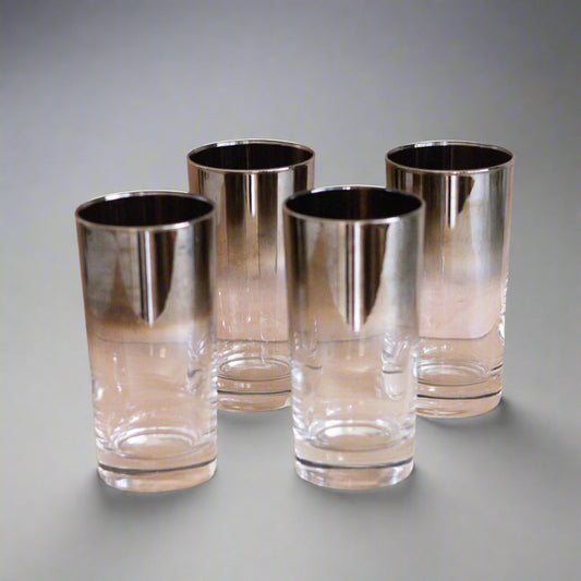 Four clear glasses with silver rims on a gray surface