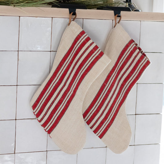 Two red and beige striped stockings hanging on a tiled wall.
