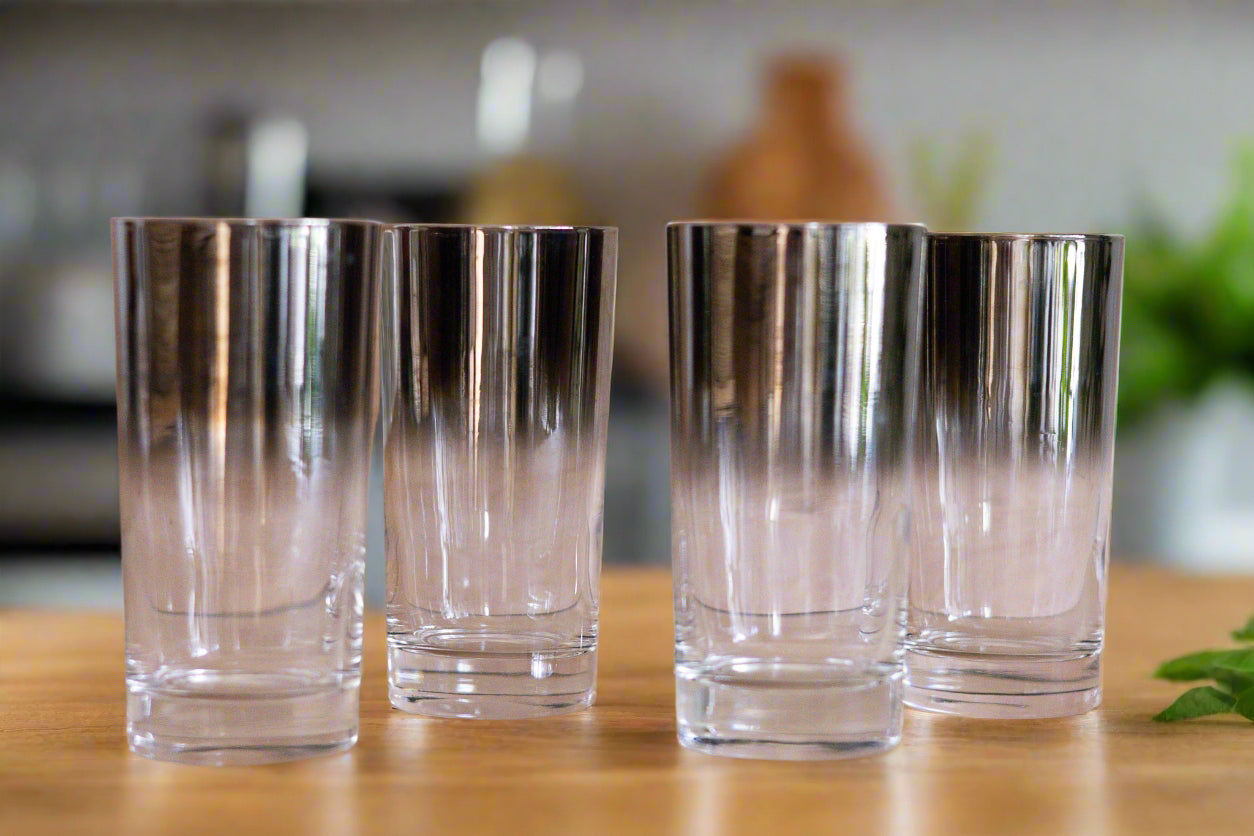 Four clear glasses with metallic gradient bottoms on a wooden surface